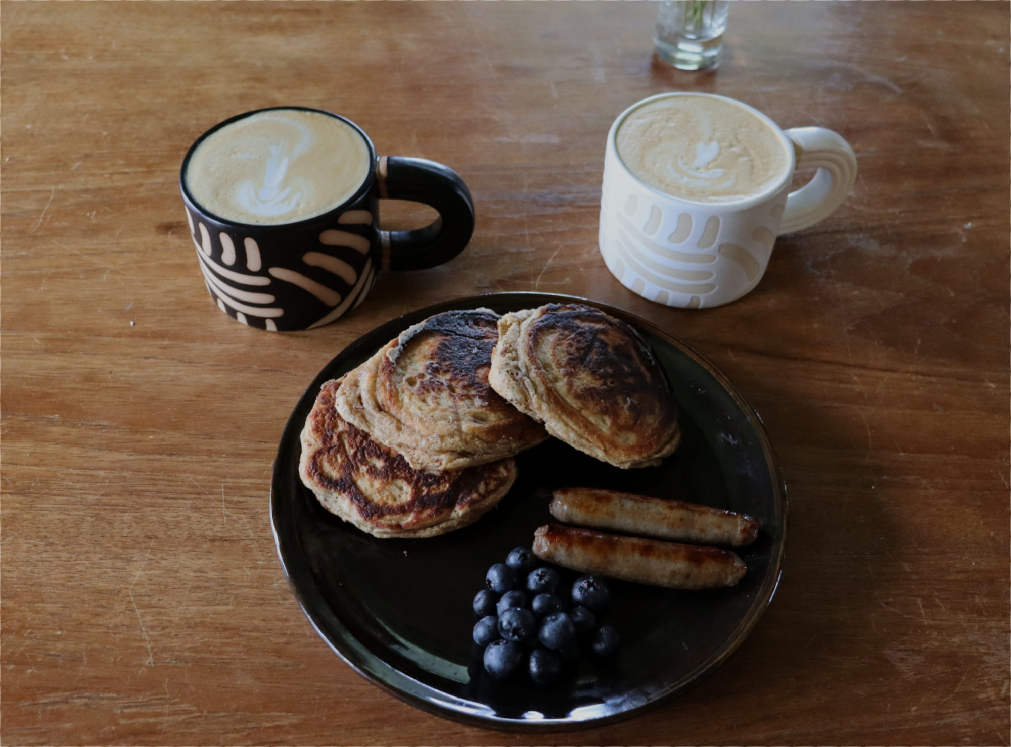 Multigrain Chai Pancakes with sausage and blueberries next to two coffee mugs