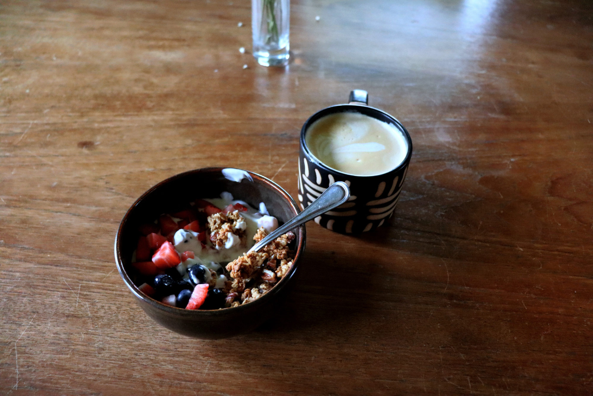 Bowl of yogurt with fruit and granola next to a ceramic mug of coffee